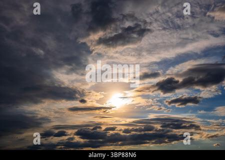 Dramatic sky background at sunset with sun shining through incoming stormy clouds. Stock Photo