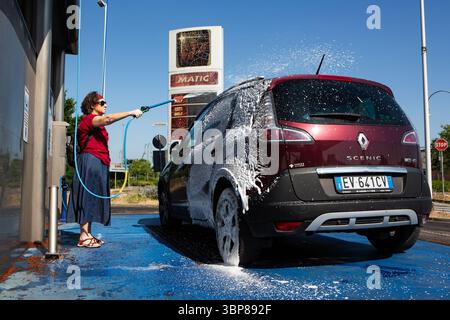 A middle-aged woman washes her sedan with precision using a high-pressure hose. Stock Photo