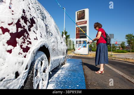 A middle-aged woman washes her sedan with precision using a high-pressure hose. Stock Photo