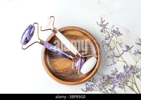 Rosa Guasha-Massagewerkzeuge in Holzschale auf Marmorhintergrund. Rosenquarz-Jaderolle. Hautpflege zu Hause, Anti-Aging und Lifting-Therapie. Ansicht Stock Photo