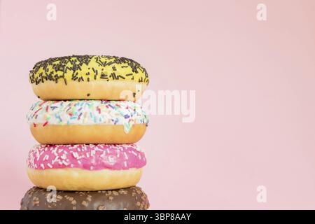 Stack of glazed sweet doughnuts with sprinkles and nuts on pink background. Copy pace for your text Stock Photo
