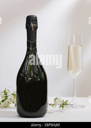Food, A dark bottle of sparkling beverage stands beside a tall flute filled with the drink. Delicate white flowers lay on the surface, creating an ele Stock Photo
