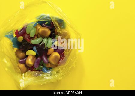 Multi-colored glazed jelly beans sweets in plastic package on yellow paper background Stock Photo