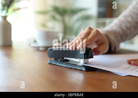 Closeup of a woman hand stapling papers on a wooden table at home Stock Photo