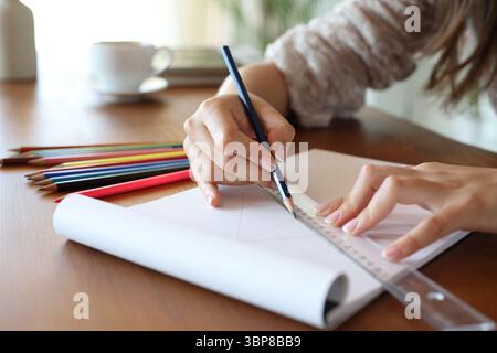 Close up of a woman hand using pencil and ruler to draw on notebook in a wooden table at home Stock Photo