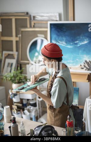 Focused creative woman artist puts final touches on piece of epoxy resin artwork in art studio. Concentrated craftswoman working details for handmade Stock Photo