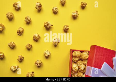 Colorful trendy backdrop with caramel popcorn and red gift box on yellow background Stock Photo