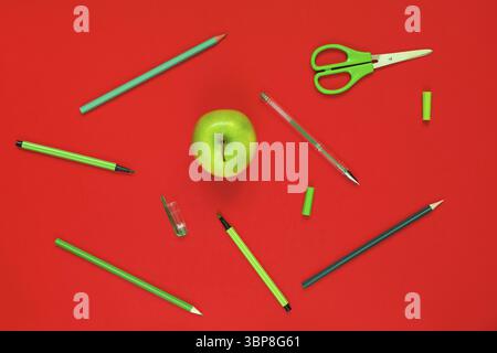 Creative flat lay of school supplies - green pens, pencils, scissors and an apple on a red background Stock Photo