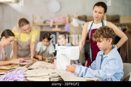 Engaged schoolboy stitching fabric on machine in sewing class Stock Photo