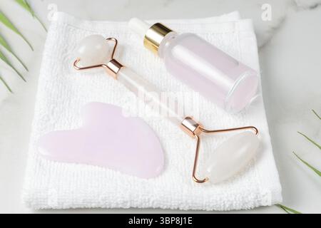 Pink quartz Gua sha scraper and roller face massager and bottle of cosmetic serum for the face on white towel Stock Photo