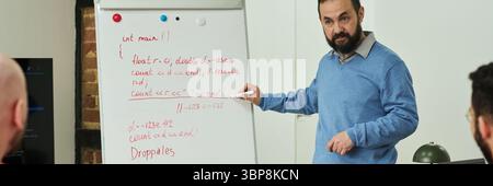 Middle aged Caucasian man teaching programming to group of prisoners, standing by flip chart with handwritten code, engaging adult male inmates in educational activity in prison classroom Stock Photo