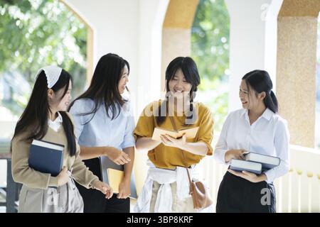 A group of college students walking together in a campus hallway, smiling and carrying books, engaging in casual conversation Stock Photo