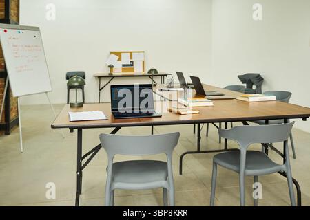 Empty classroom with several laptops, books, notebooks and writing materials arranged on tables, suggesting educational setting in prison environment with no people present Stock Photo