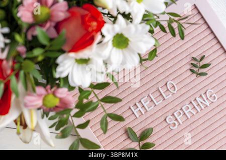 Text Hello Spring on pink letter board and bouquet of colored flowers. Concept Springtime mood and happiness Stock Photo