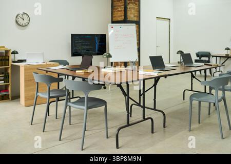 Empty classroom with several laptops, books, and notebooks arranged on tables, whiteboard and monitor displaying educational materials, setting representing prison education environment Stock Photo