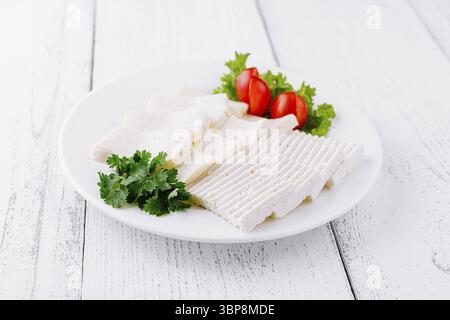 Food, White plate with sliced white cheese, cherry tomatoes, and parsley is sitting on a white wooden table Stock Photo