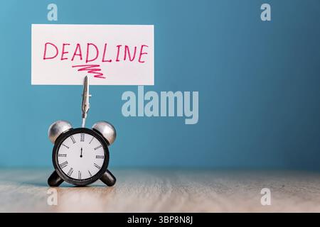 Alarm clock and banner with handwritten word deadline on wooden table. Time management concept Stock Photo