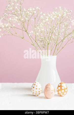 Happy Easter interior decoration. Three golden eggs and white blooming gypsoghila on pink background. Tender cozy still life Stock Photo