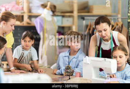 Teacher encouraging preteen girl during sewing lesson for kids Stock Photo