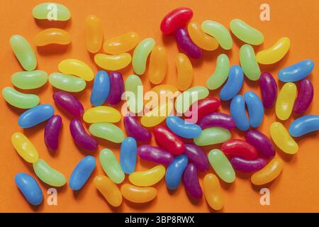 Multi-colored glazed jelly beans sweets on orange paper background Stock Photo