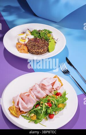 Food, Two healthy and colorful dishes with quinoa, smoked salmon, omelette and ham, served on a vibrant blue and purple background Stock Photo