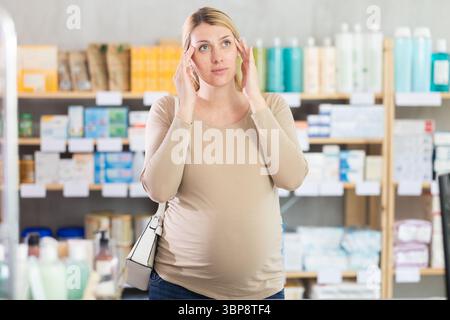 Pregnant woman visits pharmacy and suffers from headaches Stock Photo