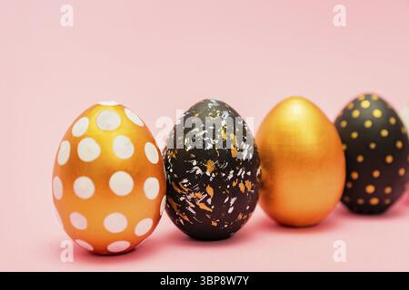 Side view of pink, white, black and golden decorated easter eggs in a row on pink background. Trendy holiday backdrop Stock Photo