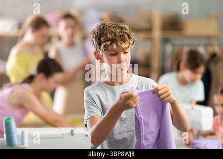 Boy checking stitched fabric at school sewing workshop Stock Photo