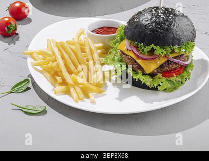 Food, A black burger sits on a white plate, topped with cheese, lettuce, tomatoes, and onions. Golden fries accompany the burger, while fresh cherry t Stock Photo