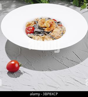 Food, A bowl of creamy seafood pasta featuring black noodles, shrimp, and cherry tomatoes sits elegantly on a textured gray surface. Fresh herbs are v Stock Photo