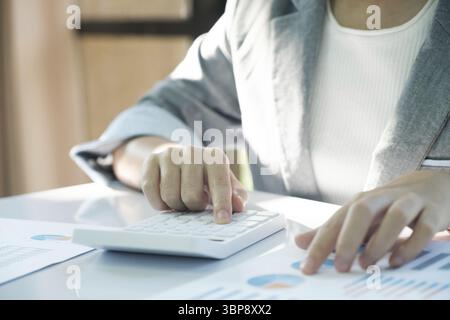 A woman is sitting at a desk with a calculator and a stack of papers. She is focused on her work, possibly working on financial or business-related ta Stock Photo
