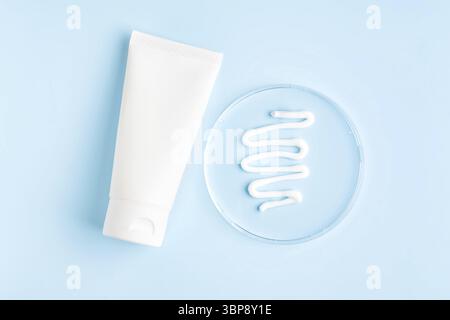 White cosmetic face cream moisturizer strokes on blue background in petri dish next to white plastic cream tube. Hygiene, skincare product with creamy Stock Photo