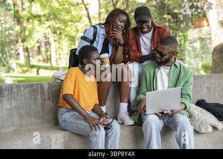 Company of relaxed thoughtful students study outside using laptop. Interested group of friends watching educational webinar, online lecture on portabl Stock Photo