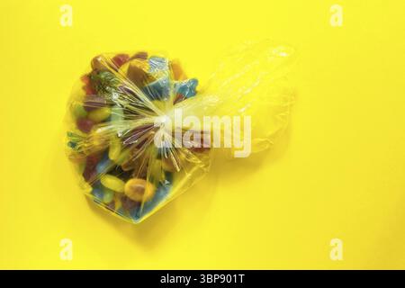 Mehrfarbige glasierte Geleebohnen Bonbons in Plastikverpackung auf gelbem Papier Hintergrund Stock Photo