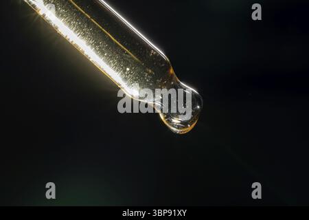 Pipette with serum, gel, oil or other cosmetic product with falling drop on black background. Macro closeup Stock Photo