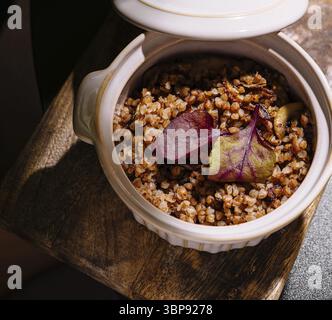 Food, Buckwheat porridge with mushrooms and beetroot leaves served in a ceramic pot on a wooden board, creating a rustic and appetizing culinary scene Stock Photo
