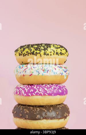 Stack of glazed sweet doughnuts with sprinkles and nuts on pink background. Copy pace for your text Stock Photo