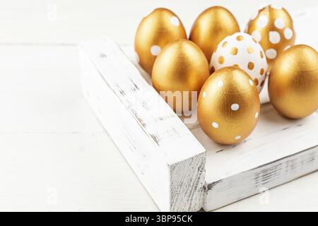 Easter festive decoration. Close up of easter eggs colored with golden paint on white wooden tray. Various dotted designs Stock Photo