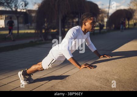 Young african-american man is exercising in the city. He is doing push-ups. Stock Photo