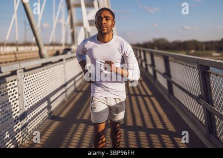 Young african-american man is jogging on the bridge in the city. Stock Photo