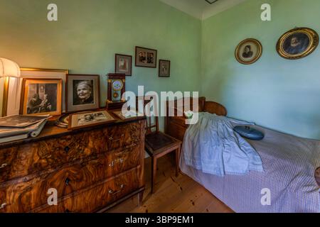 A bedroom with a chest of drawers covered in framed family portraits stands in the Mia and Hermann Hesse House in Gaienhofen, Baden-Württemberg, Germany, with a portrait photo of Mia Hesse. She was herself a professional photographer trained in Munich and Berlin, and opened a studio for portrait photography with her sister in Basel in 1902. Stock Photo