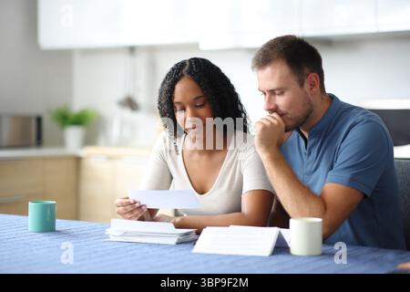 Interracial couple reading bank statement in the kitchen at home Stock Photo