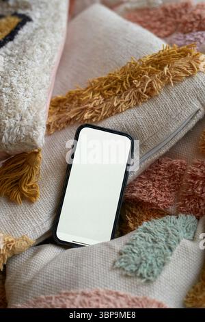 A smartphone with a blank screen rests on colorful textured pillows. Stock Photo