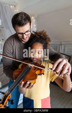 Private music teacher giving violin lessons to little girl at home ...