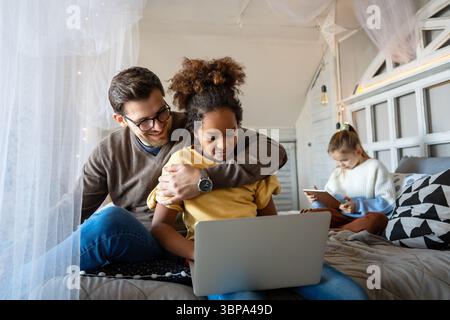 Excited single father plays with diverse, multi-ethnic daughters. Using digital tablet enjoy weekend Stock Photo