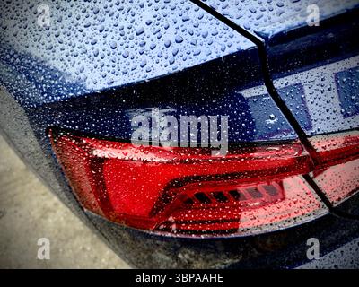 Close-up of audi car taillight with raindrops on blue painted surface, showcasing water droplets on the vehicle in an outdoor setting Stock Photo