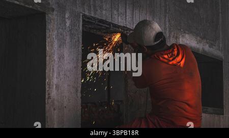 Construction worker cuts metal with a grinder, creating sparks in a concrete setting. A raw visual of hard work, precision, and real jobsite intensity Stock Photo