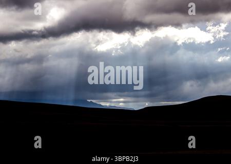 Sunrays breaking through the ominous thick clouds with distant blue mountains of the Drakensberg Mountain Range in the background. Stock Photo