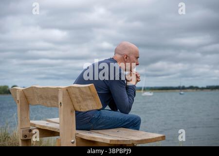 man sitting on a bench looking out to sea Stock Photo