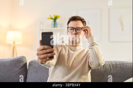 Discontent man focused in smartphone screen, looking through eyeglasses Stock Photo